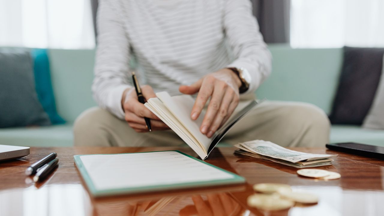 A person holding a pen over an open notebook while working out a budget