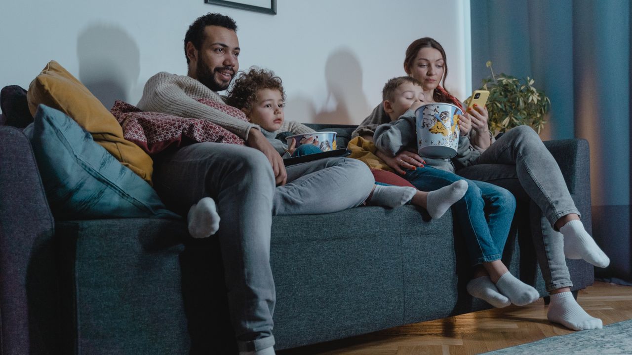 Family watching television at home in the evening while one uses a phone