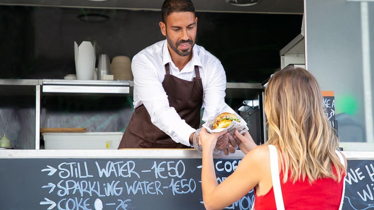 A small food business owner serving a customer at a service counter, the kind of local business that turns to Google Ads for visibility.
