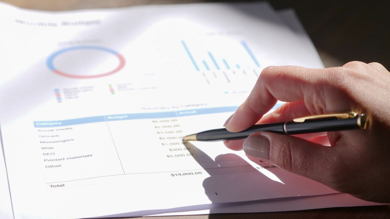 Business owner reviewing a printed budget and spreadsheet at an office desk with a calculator