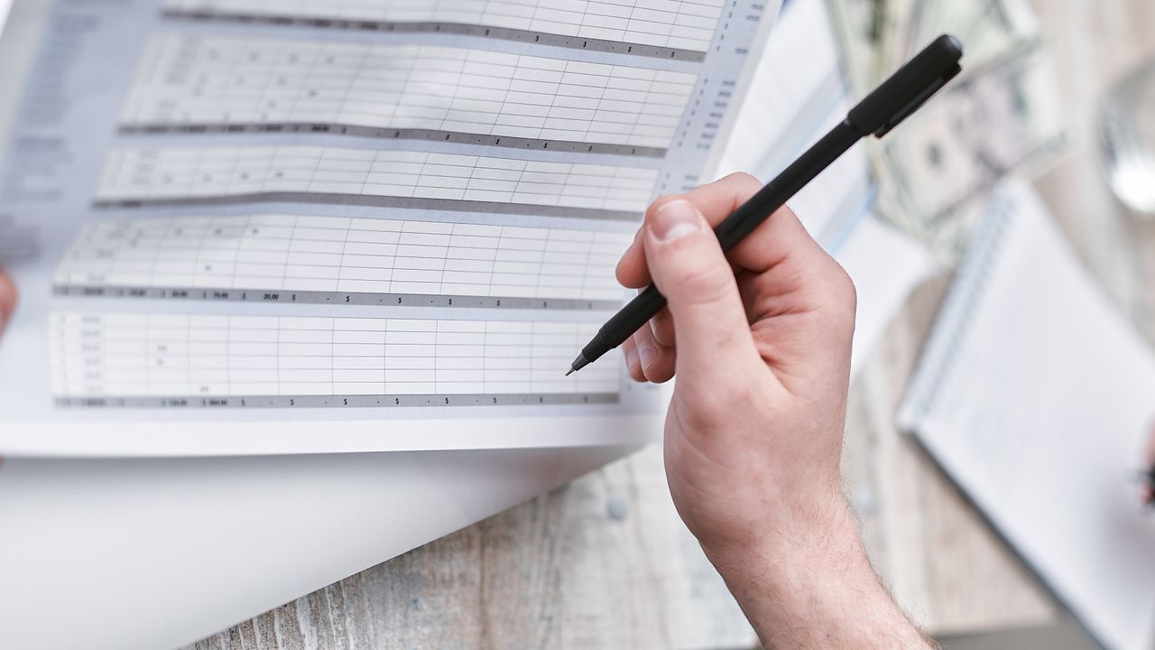 Business owner reviewing a printed budget spreadsheet at a desk with a pen and calculator