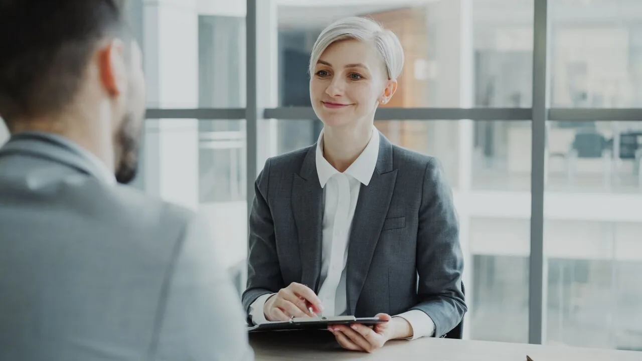 A hiring manager interviewing a candidate across a desk in a modern office